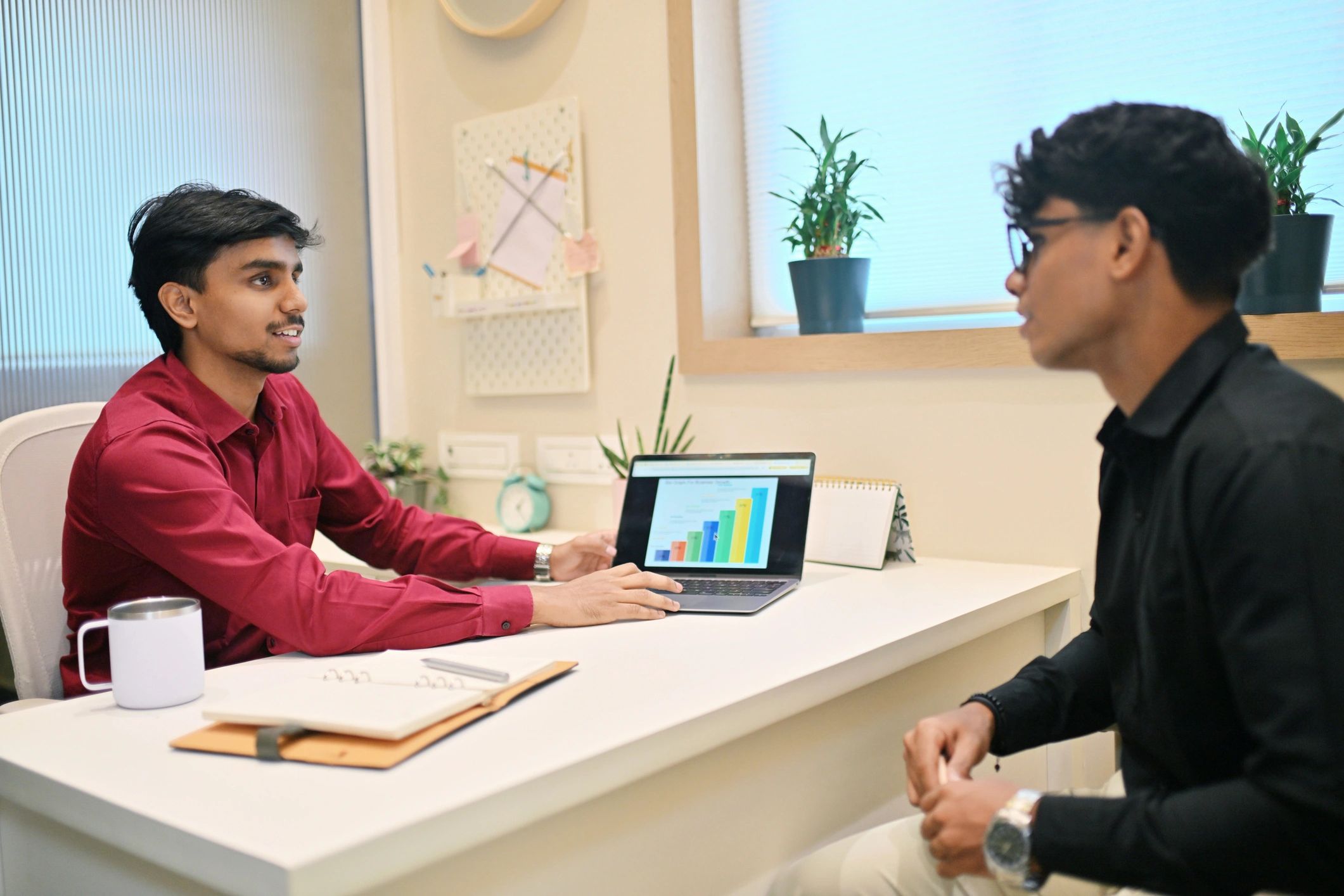 Two men sitting at a table with one of them holding a laptop.